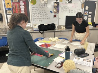 LHS Sophomores Grace Cafferky and Lola Couture, cutting fabric for a community made quilt.

